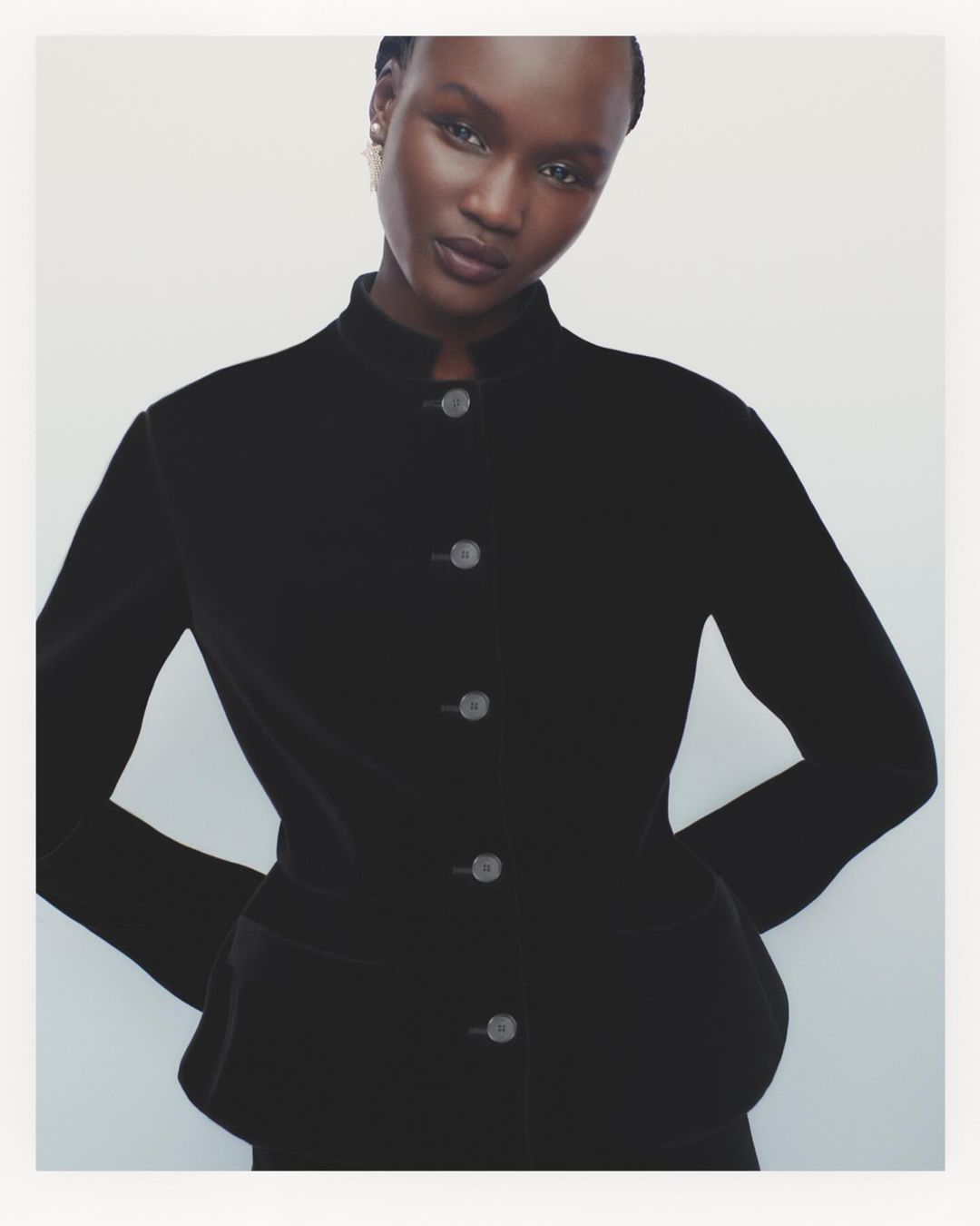 Portrait of a woman in a black blazer posing in front of a white background, showcasing fashion and beauty aesthetics.