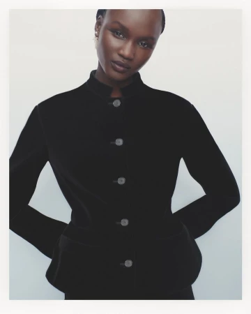 Portrait of a woman in a black blazer posing in front of a white background, showcasing fashion and beauty aesthetics.