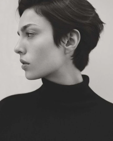 Black and white profile portrait of a woman with short dark hair wearing a black turtleneck sweater against a plain background