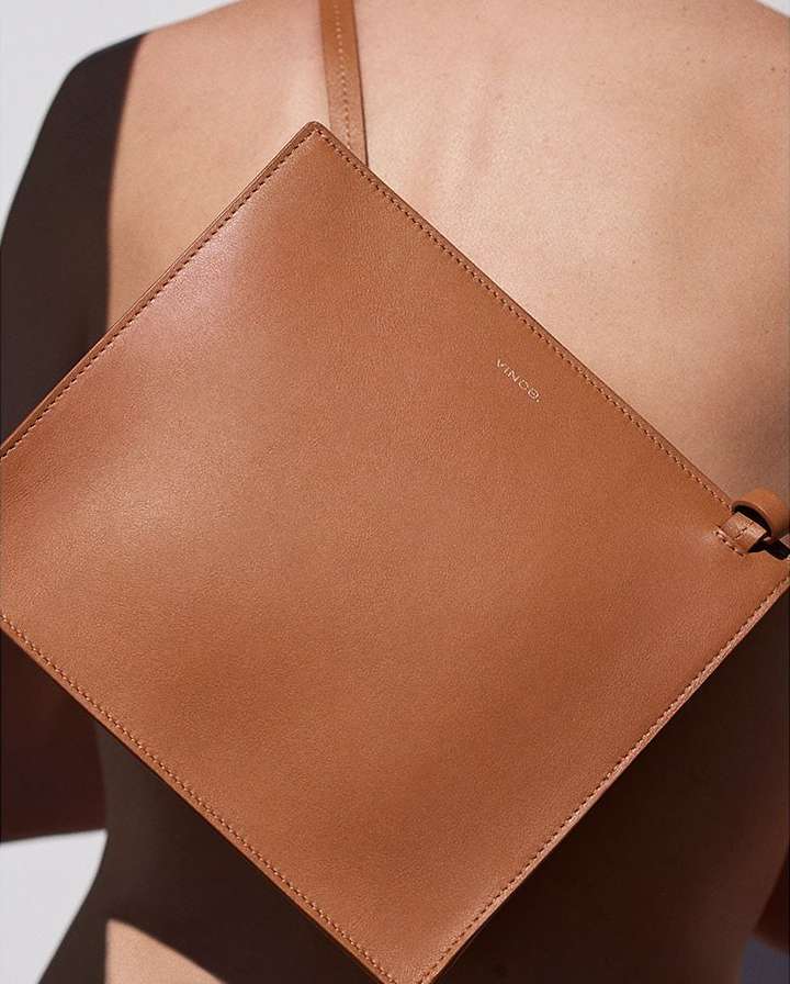 Tan leather clutch purse slung over a woman's shoulder. Close-up studio shot with soft lighting and minimalist style.
