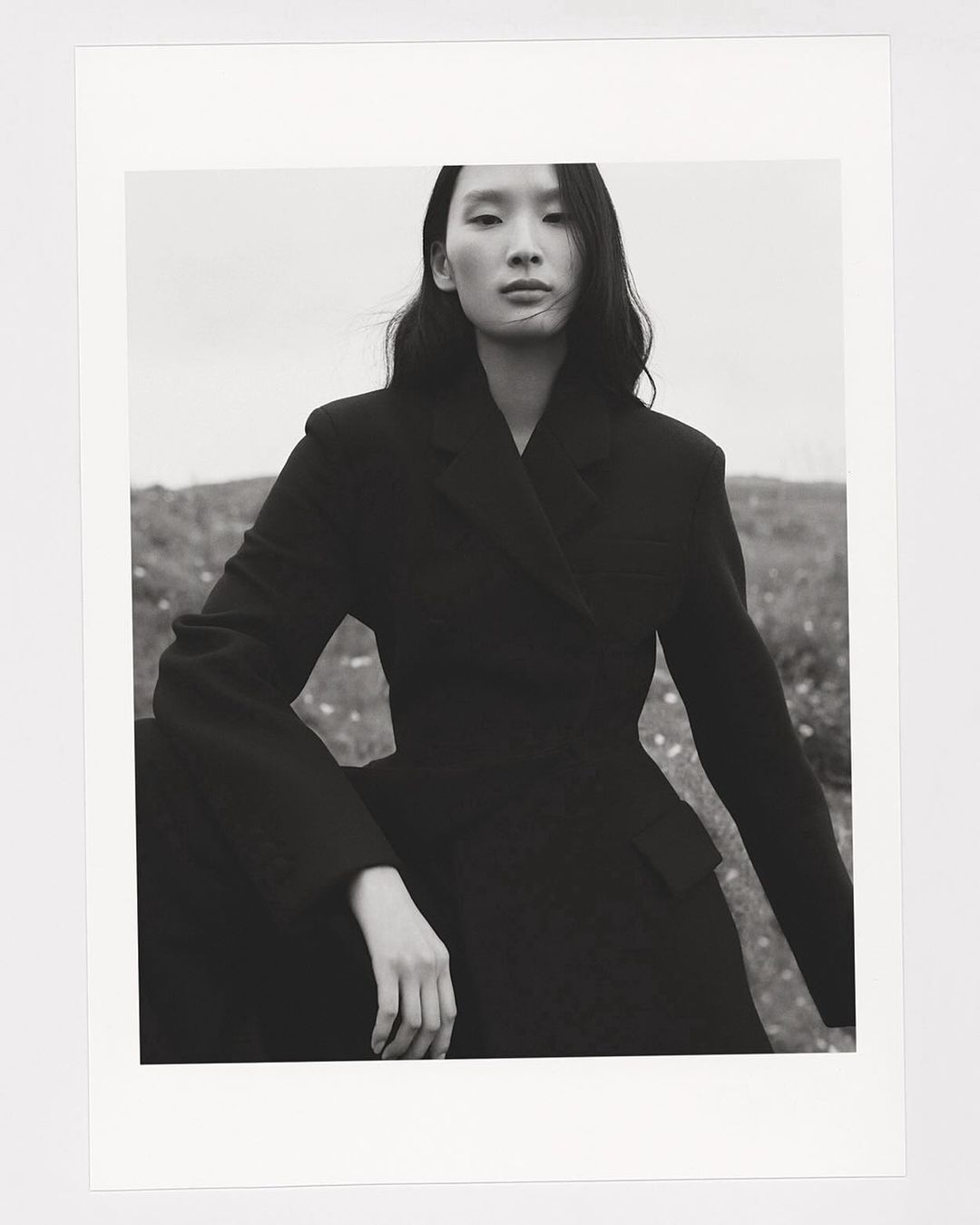 Black and white portrait of a woman wearing a dark tailored blazer outdoors against an open landscape.
