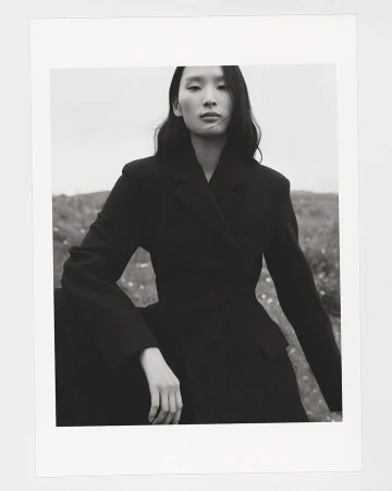 Black and white portrait of a woman wearing a dark tailored blazer outdoors against an open landscape.