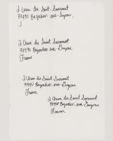 Close-up on a white sheet of paper displaying four handwritten addresses in black ink, showcasing cursive handwriting and document texture.