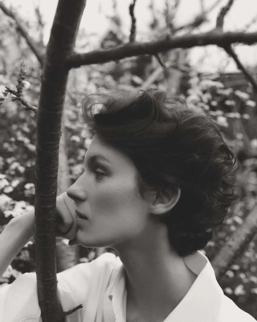 Elegant portrait of a young woman in profile, set against a backdrop of flowering trees, captured in a monochromatic, fine art style.