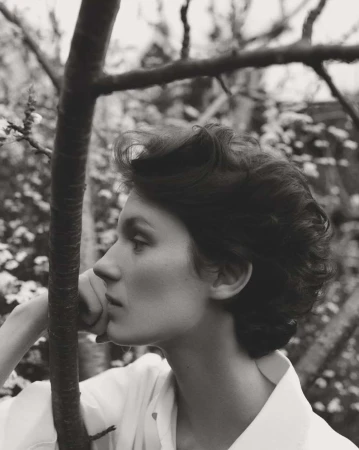 Elegant portrait of a young woman in profile, set against a backdrop of flowering trees, captured in a monochromatic, fine art style.