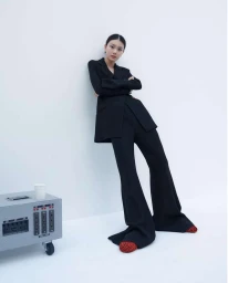 Model in black suit leaning against a white studio wall with a grey equipment case on the floor