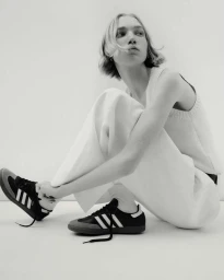 Model with bob haircut crouching against a white background wearing sneakers and light-colored knit top