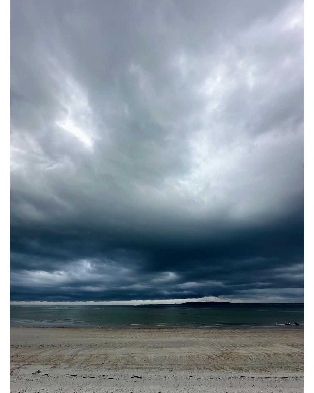 Beach scene with stormy sky. Grey, dark storm clouds above tranquil ocean and sandy beach creating a dramatic landscape.