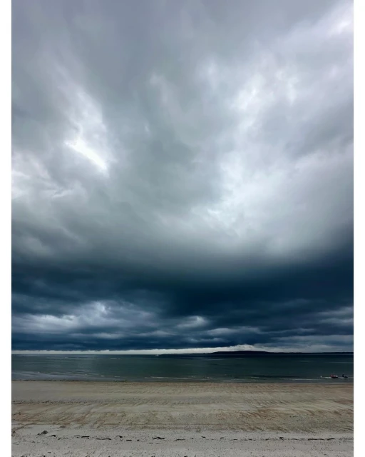 Beach scene with stormy sky. Grey, dark storm clouds above tranquil ocean and sandy beach creating a dramatic landscape.