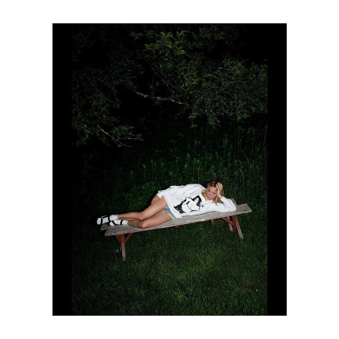 Woman lying on a wooden bench at night in a dark wooded outdoor setting by photographer Tim Barber.