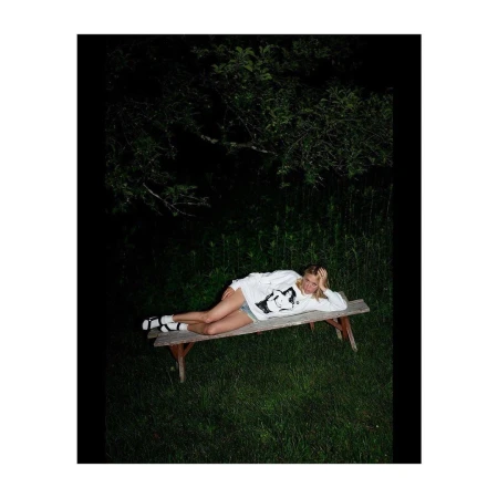 Woman lying on a wooden bench at night in a dark wooded outdoor setting by photographer Tim Barber.
