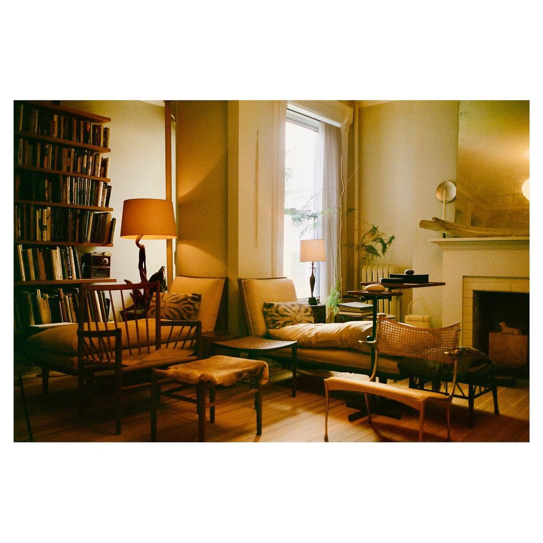 Living room interior with a bookcase, tan sofa and chairs, lamps, and fireplace, creating a warm and inviting home environment.