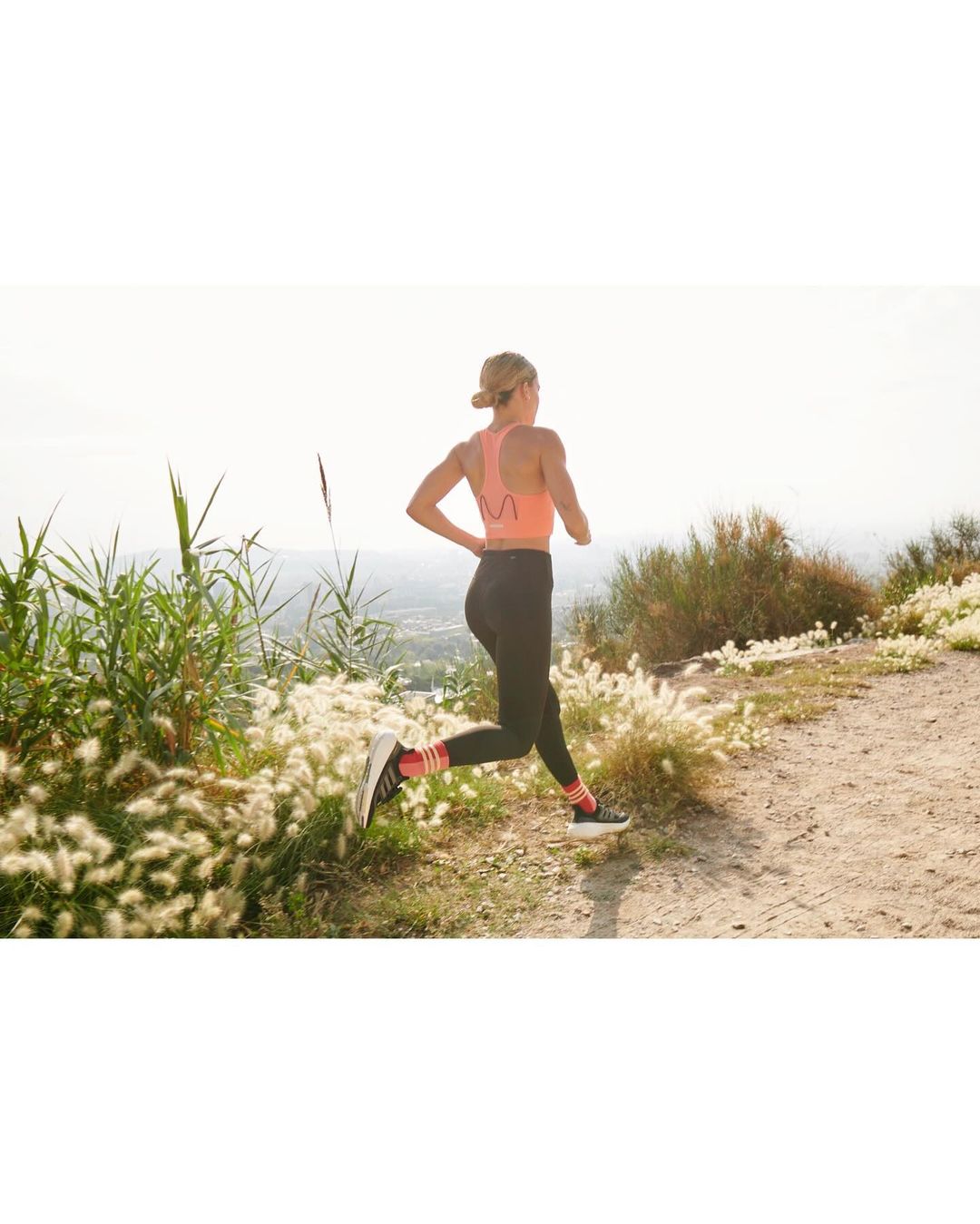 A woman in athletic wear runs on a sunny outdoor trail, showcasing fitness and an active lifestyle against a natural backdrop.