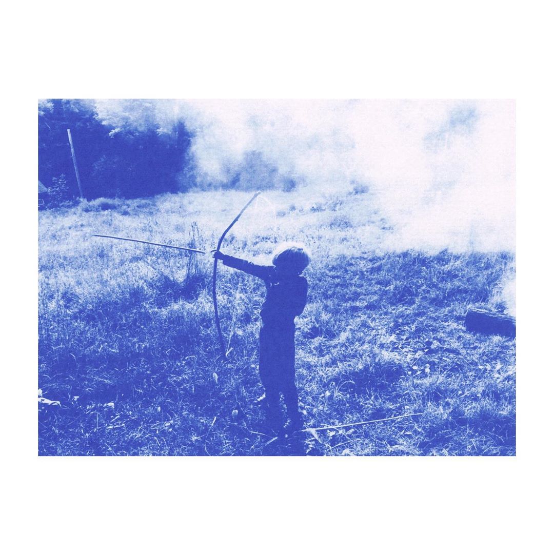 A person in silhouette, clad in dark clothing, stands in a grassy field aiming a bow and arrow toward the horizon, monochrome style.