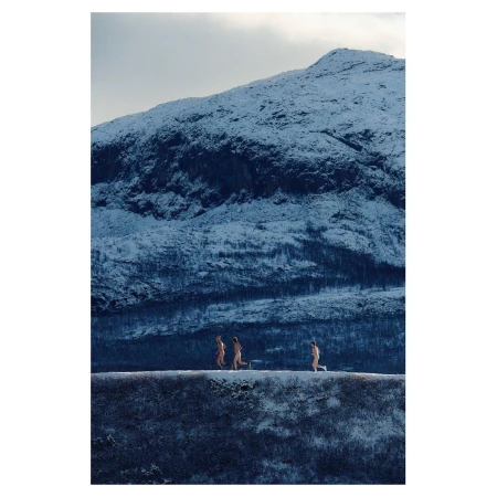 Three adult figures running in a snow landscape against a backdrop of a mountain covered in snow under an overcast sky.