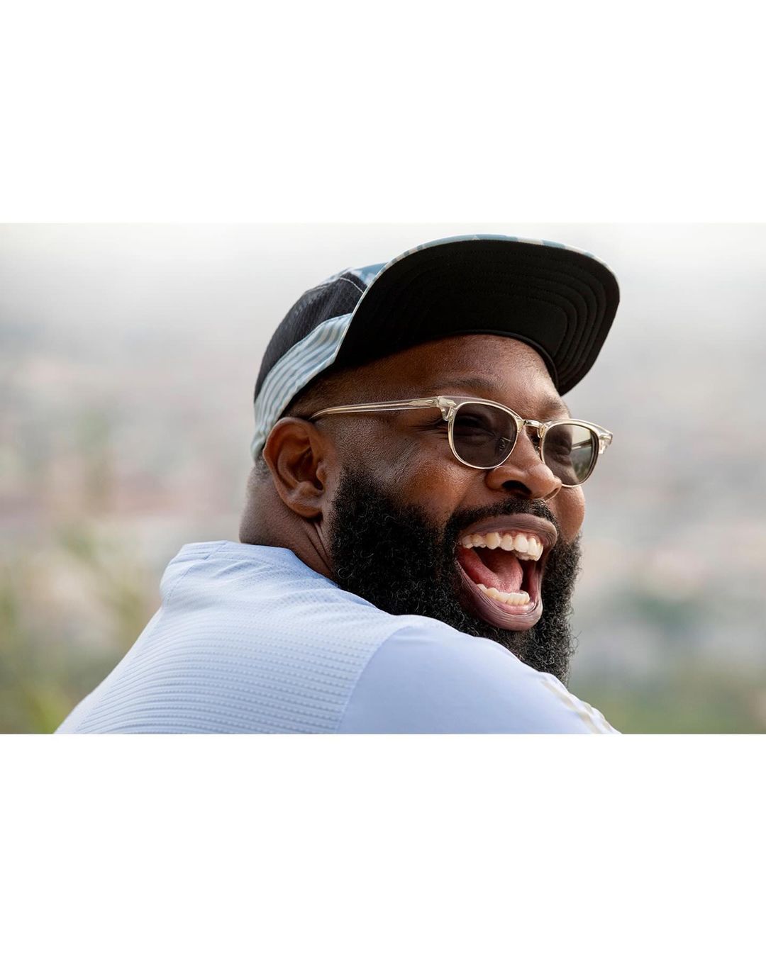 Portrait of a laughing black man wearing sunglasses and a cap by photographer Tim Barber.