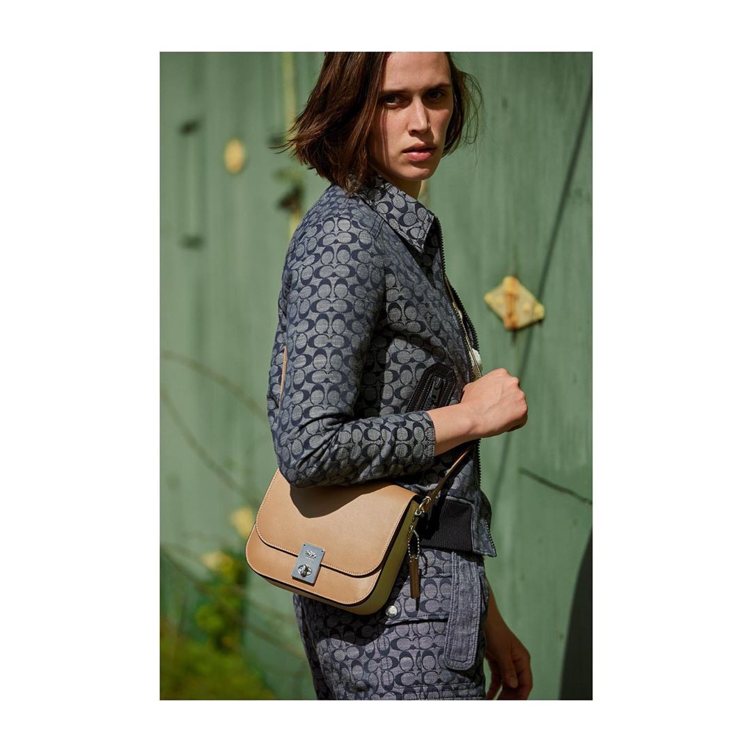 Fashion shot of a female model wearing a matching patterned jacket and pants, posing with a satchel purse in an outdoor setting.