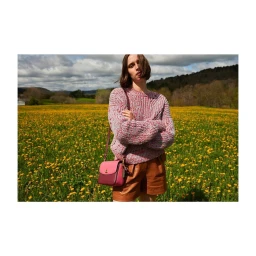 Woman wearing a chunky knit sweater and brown shorts standing in a yellow wildflower field with a pink leather handbag