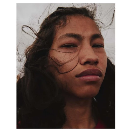 Close-up portrait of a person with dark hair blowing in the wind under an overcast sky, captured by photographers Ward and Kweskin