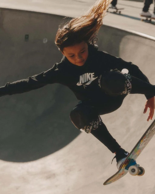 Young skateboarder soars in a concrete skatepark, wearing Nike sportswear, catching air on a skateboard, and showing movement and style.