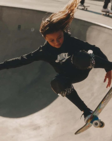 Young skateboarder soars in a concrete skatepark, wearing Nike sportswear, catching air on a skateboard, and showing movement and style.