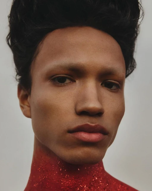 Close-up portrait of a person with dark hair and light skin, wearing a sparkly red garment around their neck, neutral background.