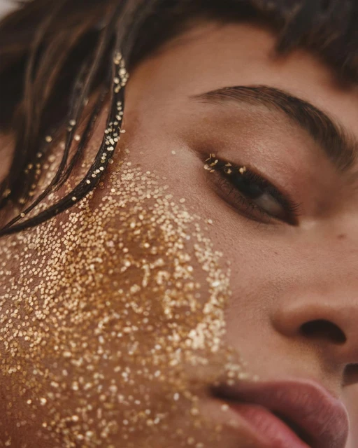 Close-up portrait of a person with glitter makeup on their face and in their hair, focusing on the details of the glitter and skin texture.