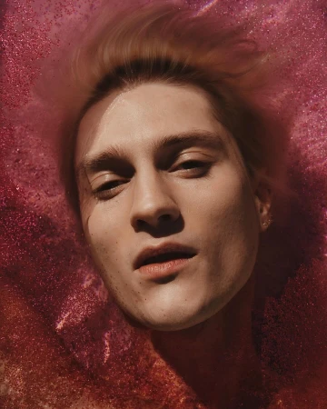 Close-up portrait of a man submerged in shimmering magenta water with floating glitter particles by photographers Ward & Kweskin.