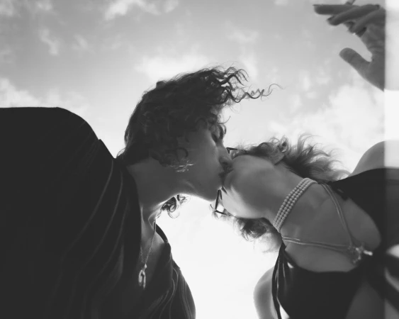 Low-angle monochrome portrait of a couple kissing outdoors under an open cloudy sky, shot by Ward and Kweskin.
