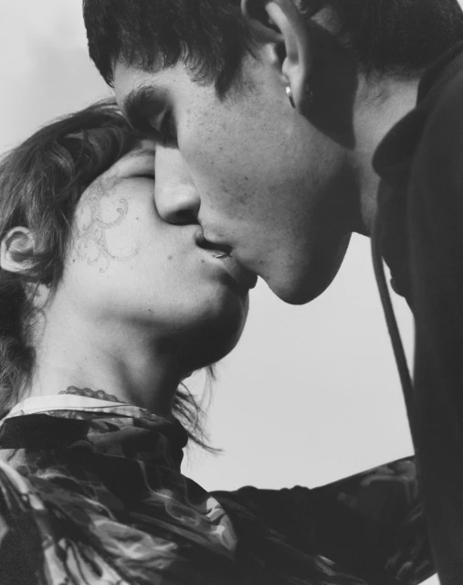 Black-and-white portrait of two people kissing in a close-up, showcasing their facial features and the intimate nature of the moment.