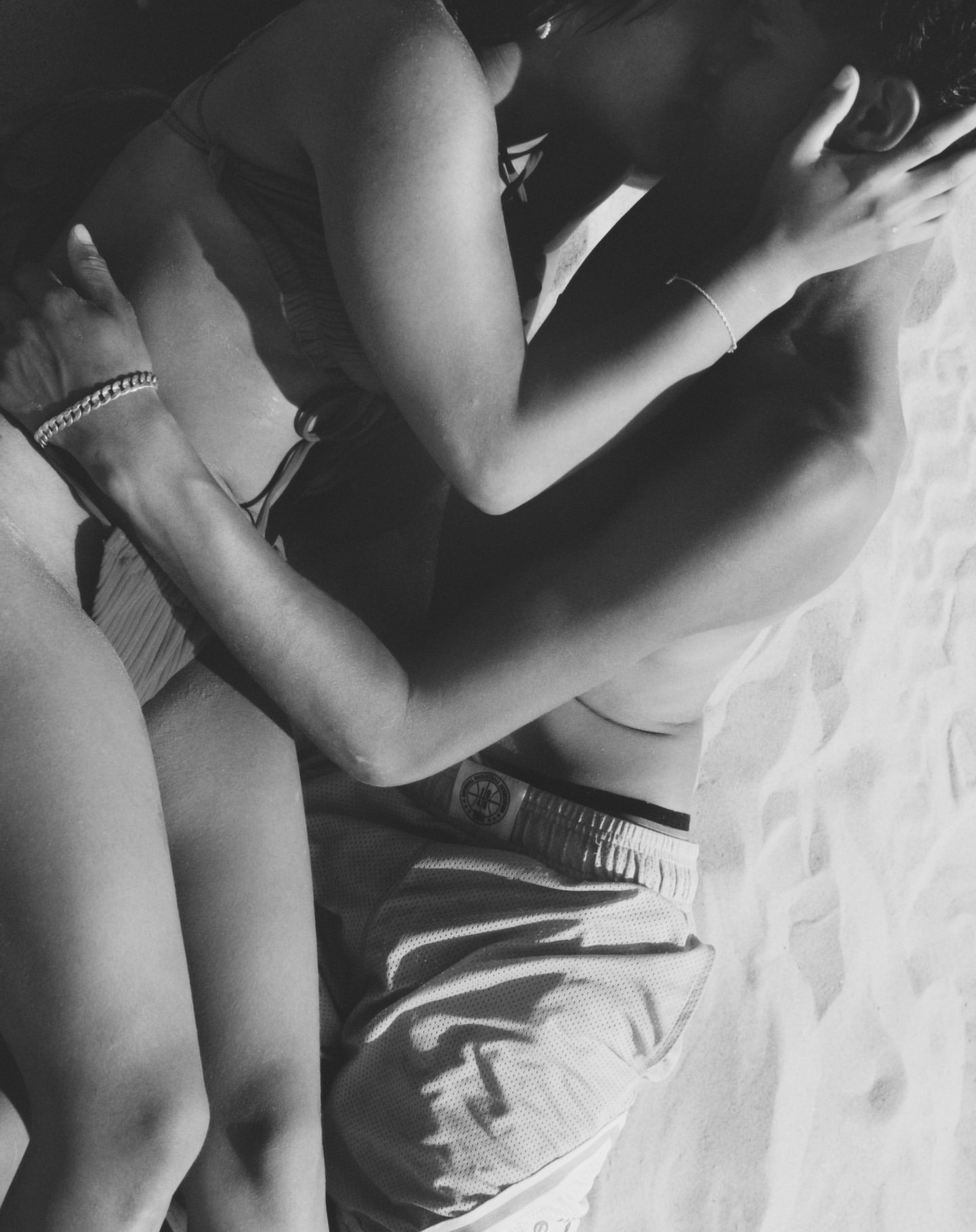 Close-up black and white portrait of a man and woman embracing intimately on a sandy surface, photographed by Ward & Kweskin.