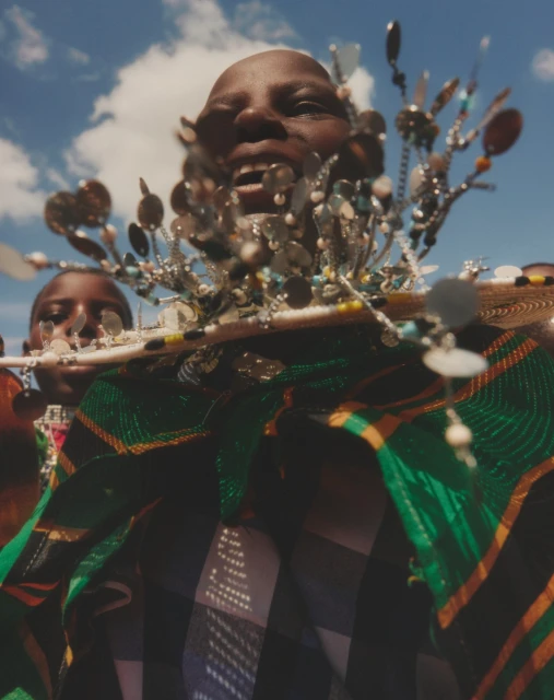 Close-up of an adult with jewelry in outdoor shot, with a bright sky and clouds. Decorative green and black material is visible.