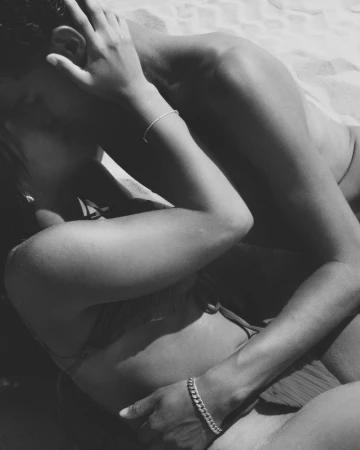 Close-up black and white photograph of two people embracing on a sandy beach by photographers Ward and Kweskin.