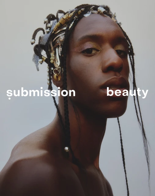 Close-up portrait of an adult with dark skin and braids wearing decorative headwear in front of a light gray seamless background.