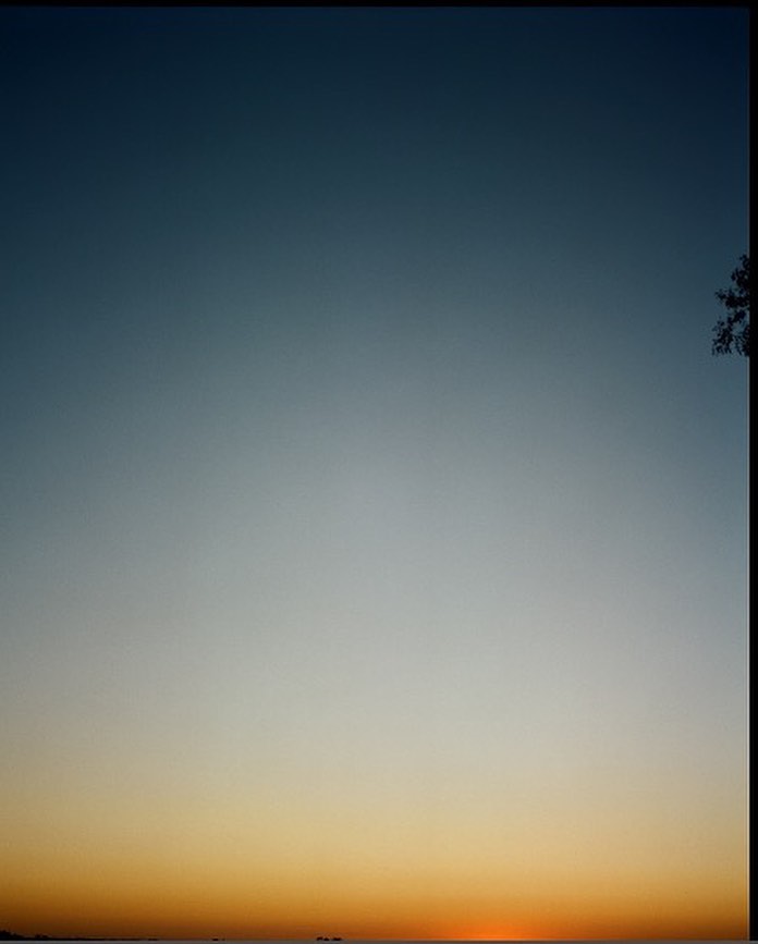 A captivating sunset sky gradient blending from orange to light blue, over a calm sea with distant silhouettes of ships, evoking tranquility.