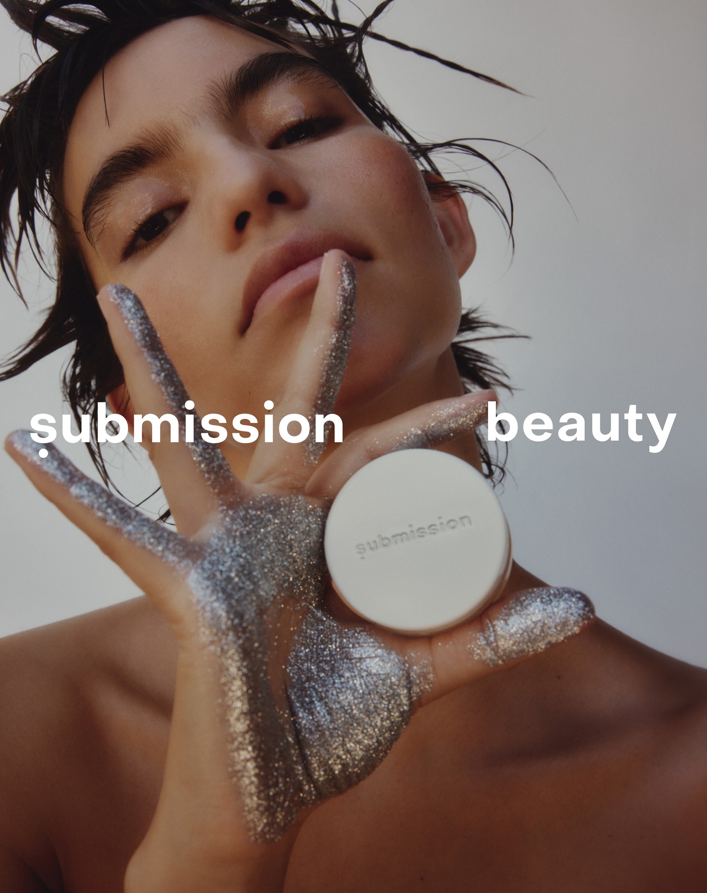 Close-up of a woman with silver glitter on her hand holding a beauty product, set against a neutral backdrop. Beauty advertisement.