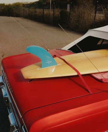 A classic red convertible car with a surfboard strapped to the back, highlighting vintage automobile design and surf culture.
