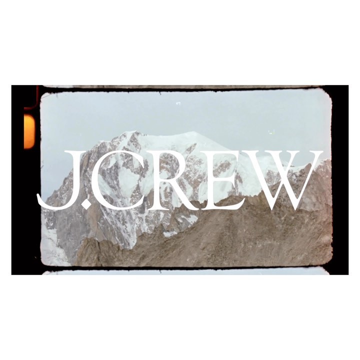 Snow-covered mountain range with a dramatic peak, set against a pale sky, creating a cool and scenic outdoor vista. J.Crew logo.