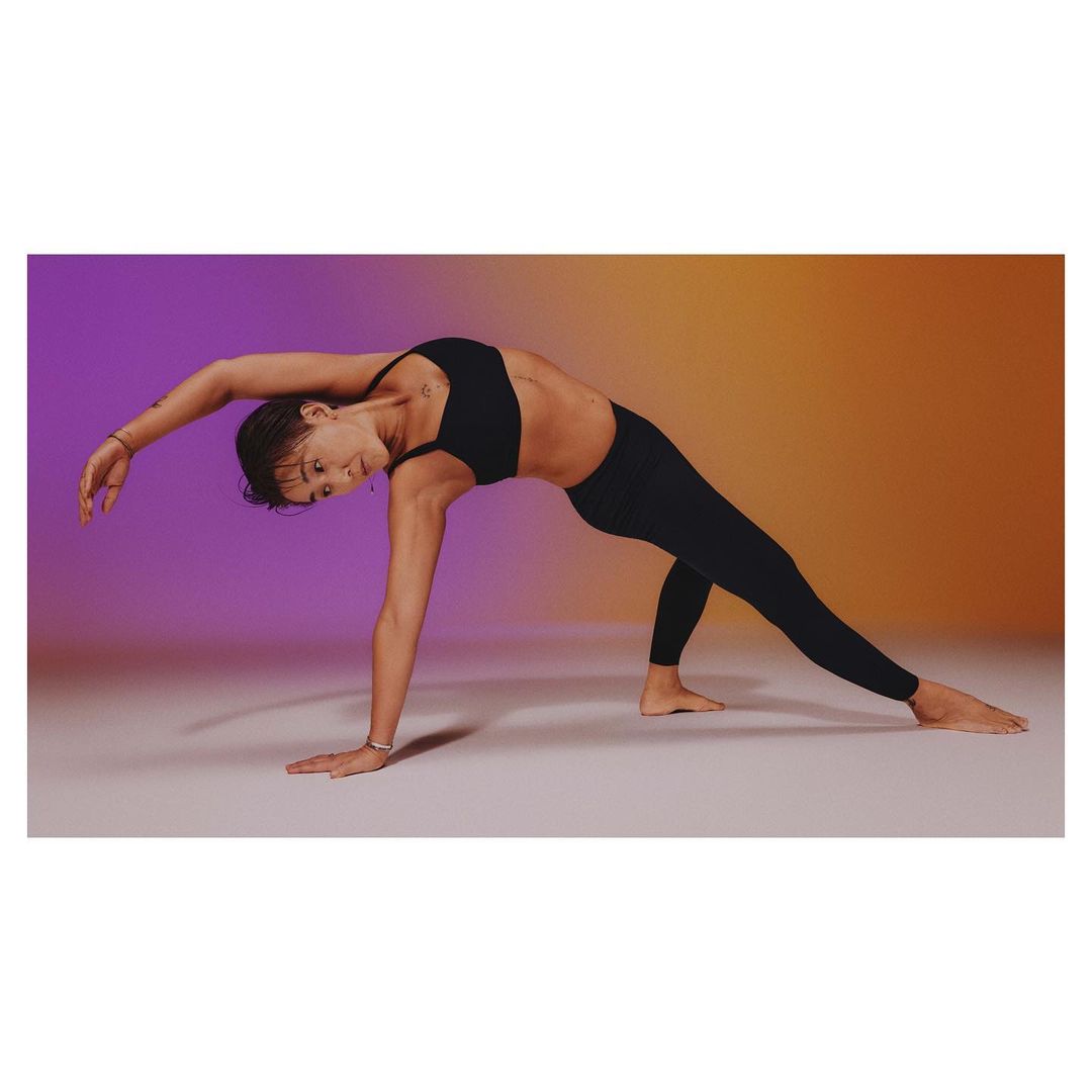 Athletic woman in black workout clothes performing a yoga pose on a gradient background, displaying fitness and flexibility.