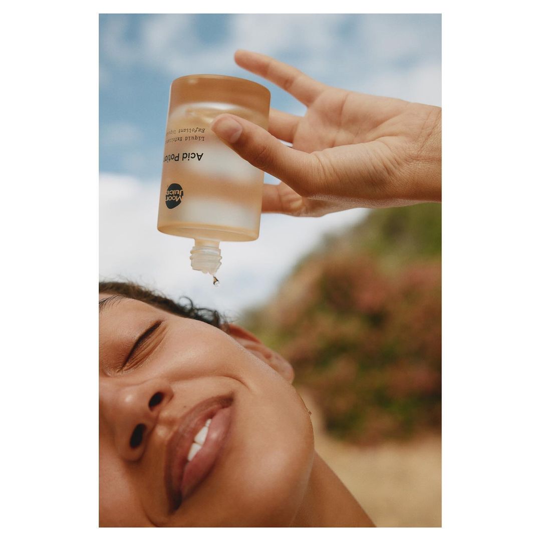 Close-up of an adult woman smiling as cosmetic product is poured on her face outdoors, showcasing beauty and skincare.