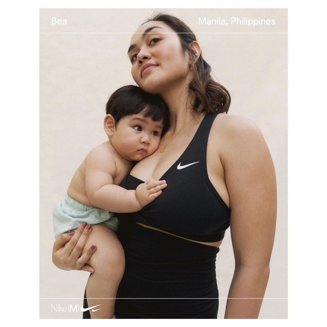 Adult woman in sports bra holding baby indoors. Mother and child portrait in front of a neutral background, close up shot.