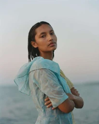 Portrait of a woman with wet hair wearing a light blue patterned dress standing near water at dusk
