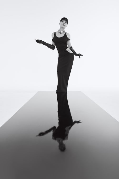 Woman in black dress with long gloves standing on a reflective black runway against a white background
