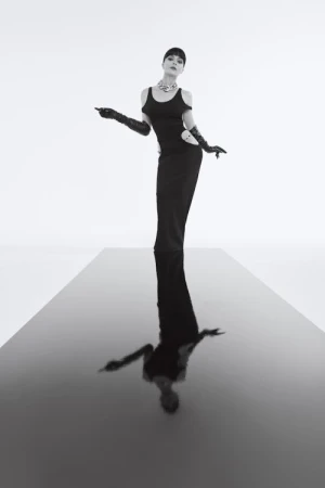 Woman in black dress with long gloves standing on a reflective black runway against a white background