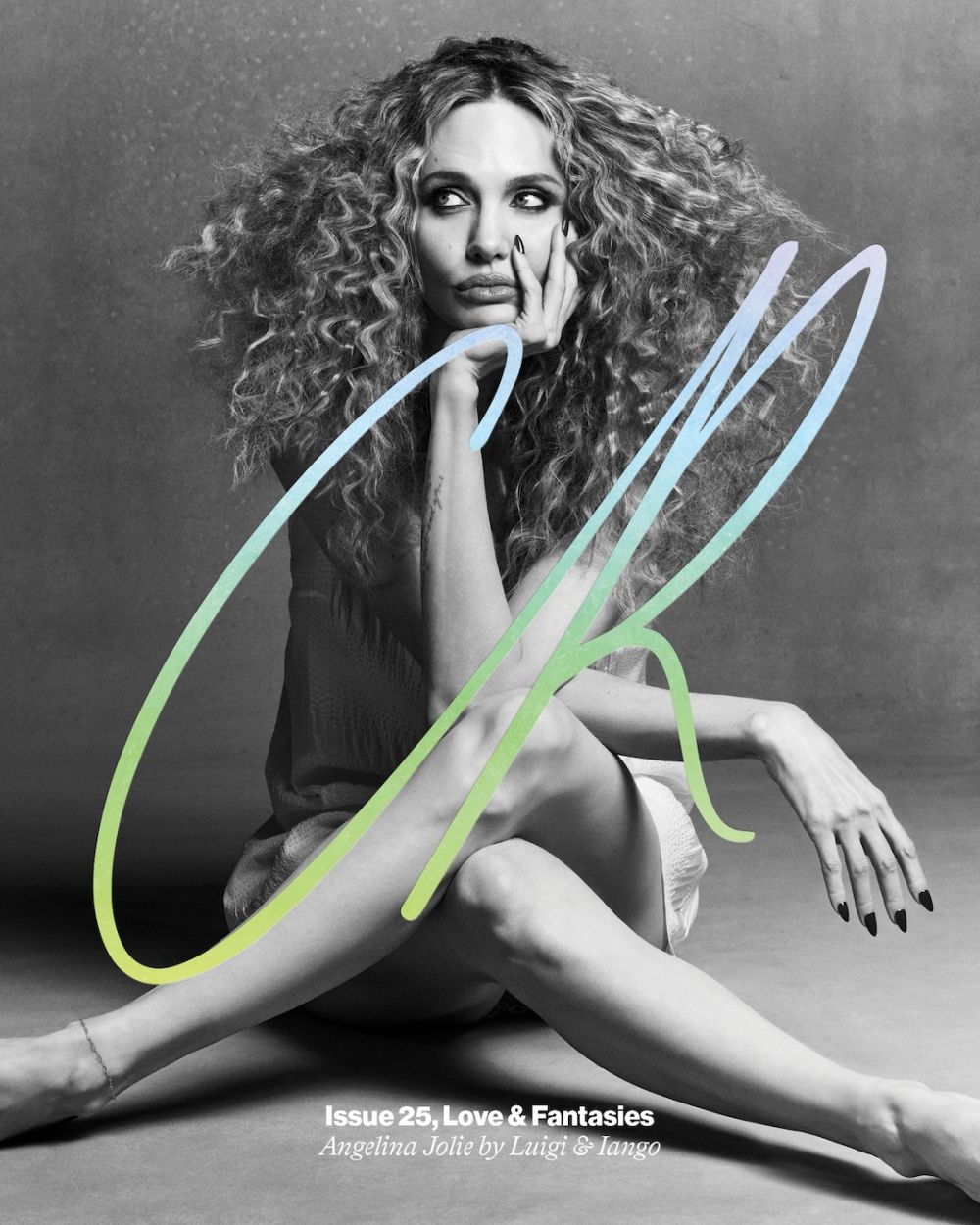 Angelina Jolie poses with expressive curly hair, neutral makeup, and black nails in a black and white magazine-cover style portrait.