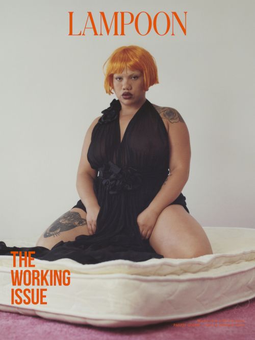 Magazine cover featuring a woman with orange hair wearing a black dress, kneeling on a mattress in a studio setting with a pink floor.