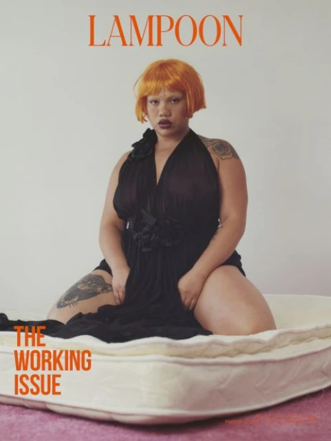 Magazine cover featuring a woman with orange hair wearing a black dress, kneeling on a mattress in a studio setting with a pink floor.