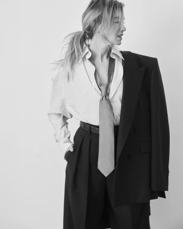 Black and white portrait of a blonde woman in a striped shirt, tie, and suit jacket draped over her shoulder.
