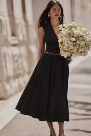 Elegant Asian woman in black dress holds a white floral bouquet outdoors against a neutral building backdrop, complemented by hoop earrings.