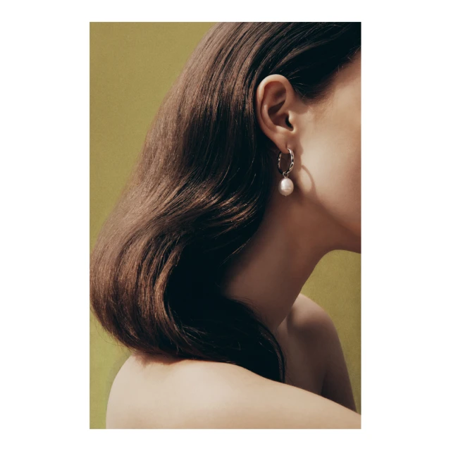 Close-up shot of a woman with wavy brunette hair wearing pearl hoop earrings against a light green background in a beauty context.